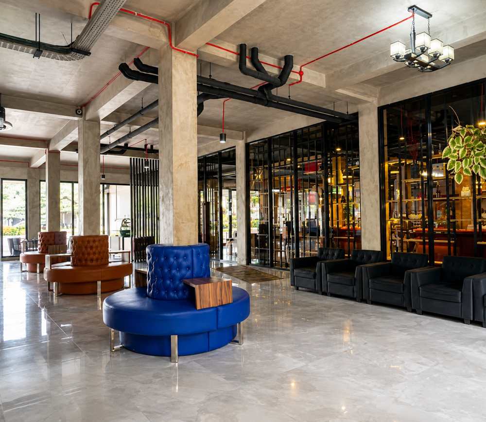 Lounge bersama dengan kursi bundar berjahit tuft, kursi santai, dan lampu gantung di samping area makan berdinding kaca