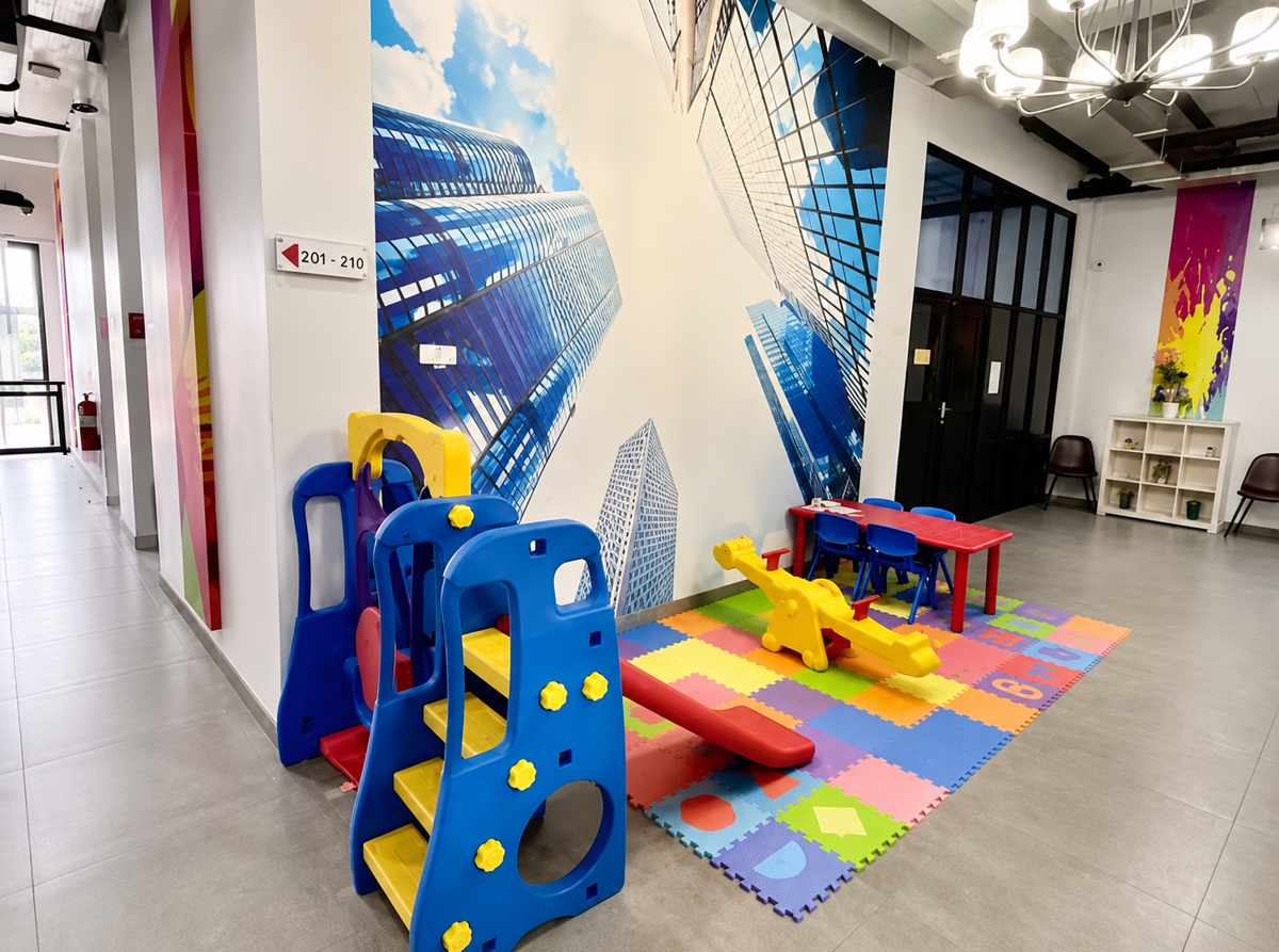 Area bermain anak dengan perosotan, jungkat-jungkit, dan matras lunak di lorong bermural