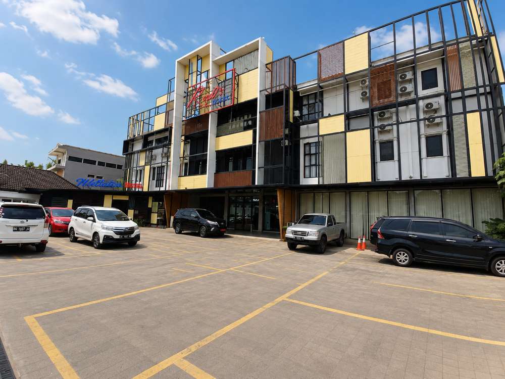 Eksterior hotel dengan fasad kuning dan kayu terlihat melintasi area parkir pribadi yang bertanda