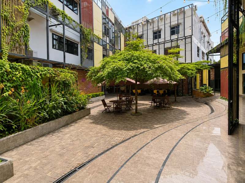 Halaman taman hotel dengan pohon peneduh, payung, dan tempat duduk teras di antara dinding bertanaman